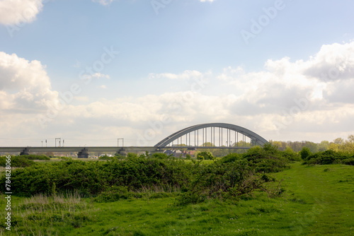 Spring landscape with green grass meadow along the Lek river, De Kuilenburgse spoorbrug (The Culemborg railway bridge) cross the river in a small village in the Dutch province of Utrecht, Netherlands. © Sarawut
