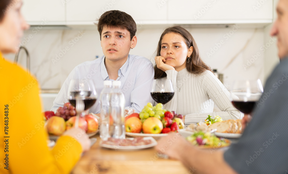 Upset guy with wife visiting parents. Young couple sitting with glasses of wine at family holiday table