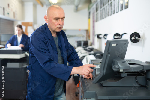Caucasian man working in printing office, using large format printer.