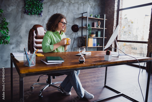 Photo of cheerful lovely relaxed woman enjoying morning tasty coffee looking monitor modern office workspace workstation