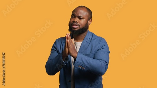 Friendly african american man puts hands together in apology gesture, asking for forgiveness. Apologetic BIPOC man doing sorry gesturing, asking for pardon, isolated over studio background, camera A