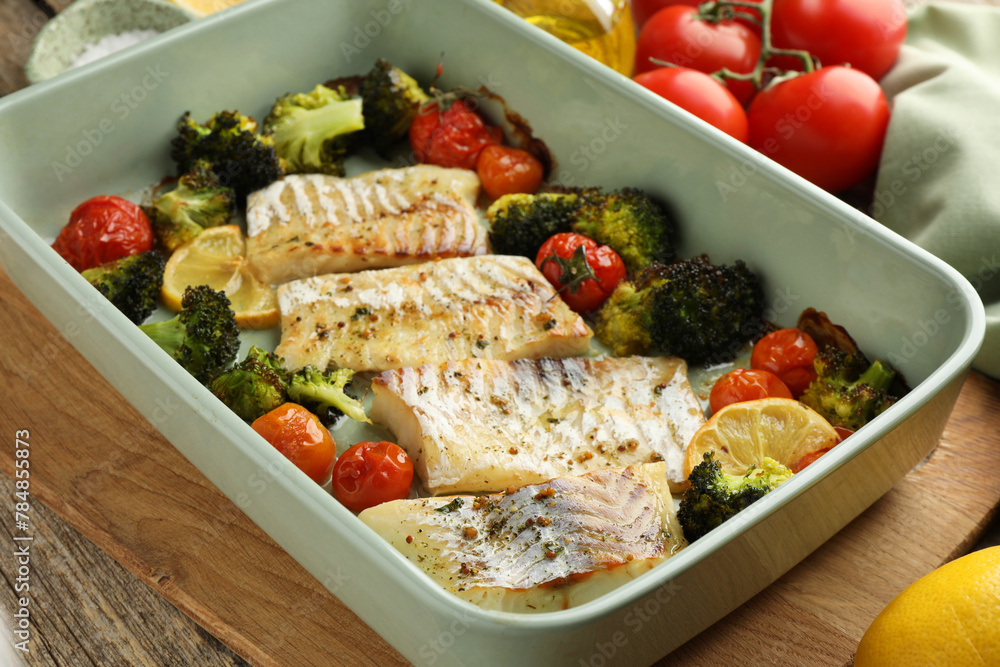 Pieces of delicious baked cod with vegetables, lemon and spices in dish on wooden table, closeup Pieces of delicious baked cod with vegetables, lemon and spices in dish on wooden table, closeup