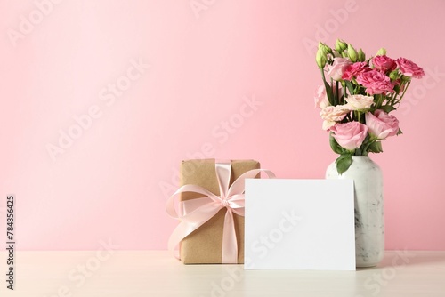 Happy Mother's Day. Gift box, blank card and bouquet of beautiful flowers in vase on white table against pink background. Space for text © New Africa