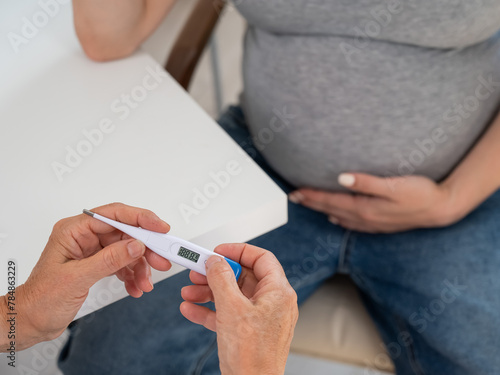 A pregnant woman visits a doctor. Therapist holding an electronic thermometer. 