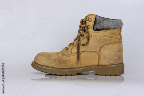 One worn old yellow hiking trekking lace boots Isolated on white glossy surface with beautiful reflection effect. Second hand tourist walking shoes. Side view. Copy Space. White background.