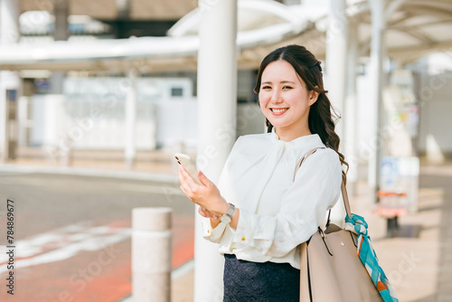 駅・ステーションのロータリーでスマホを使う女性（アプリ・モバイルチケット・チケットレス・電子乗車券） 