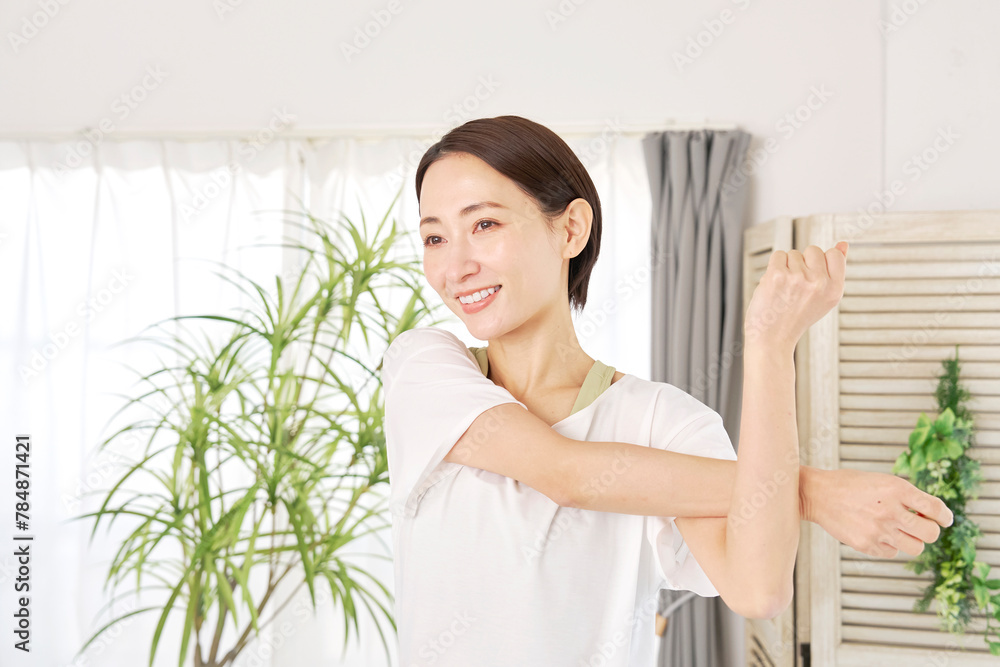 自宅で腕のストレッチをする40代の女性 自宅で腕のストレッチをする40代の女性
