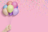 Female hand holds bunch of colorful balloons on pink background with confetti. Empty space for text