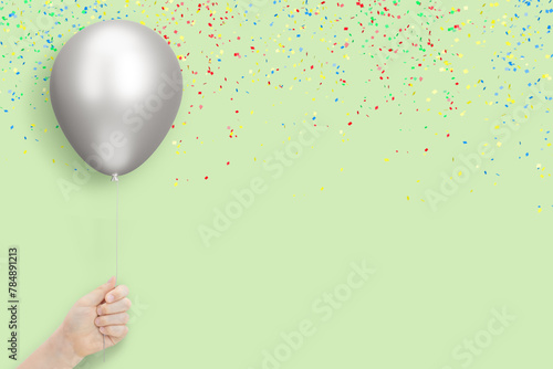 Female hand holds silver balloon on mint background with confetti. Empty space for text