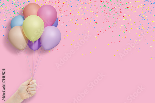 Female hand holds bunch of colorful balloons on pink background with confetti. Empty space for text