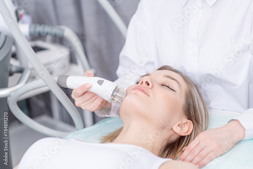 Pretty young woman client lying with closed eyes and getting stimulating beauty facial treatment during rf-lifting and vacuum massage procedure at clinic. Radiofrequency face lifting