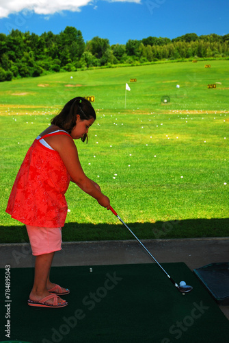 A young girl stakes her stance at a driving range, ready to tee off on a sunny summer day