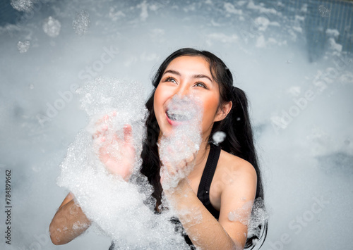 Portrait of pretty young woman in bikini having fun on soap foam disco party in the swimming pool..