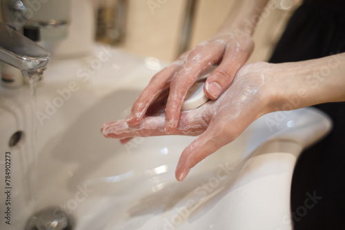 A bar of soap in soapy hands near the water tap in the sink