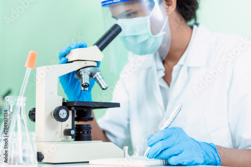 Indian Scientist man look into Microscope research in science laboratory. Asian biochemistry scientist using microscope in laboratory chemistry labs. Covid-19 medical research scientific experiment