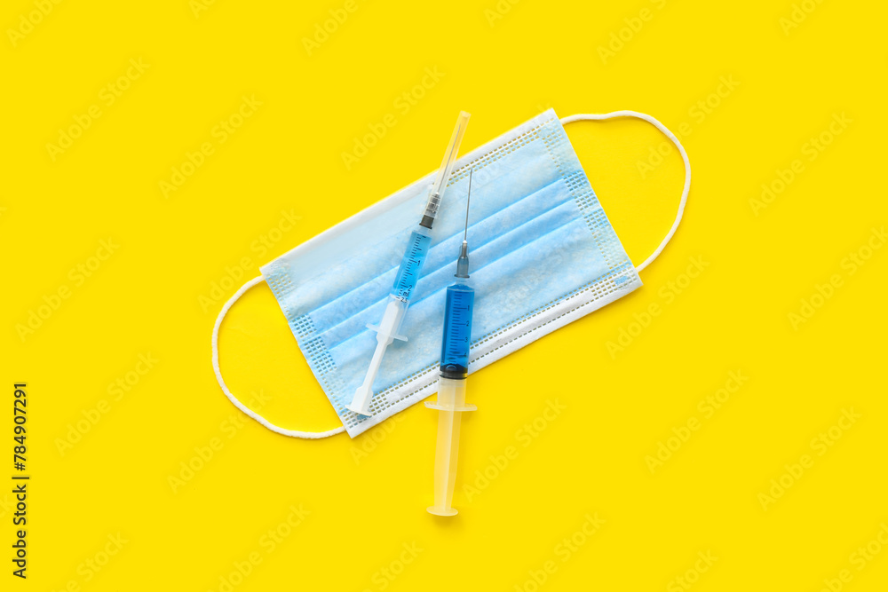 Medical syringes with medicine and mask on yellow background