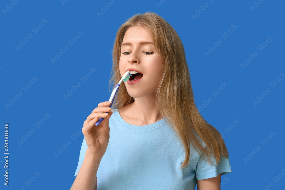 Young woman brushing her teeth on blue background Young woman brushing her teeth on blue background