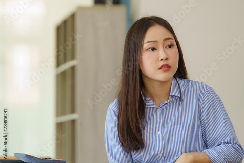 Young Asian businesswoman looking seriously outside the window while sitting at a desk. Serious confident Asian woman looking away and dreaming of success.
