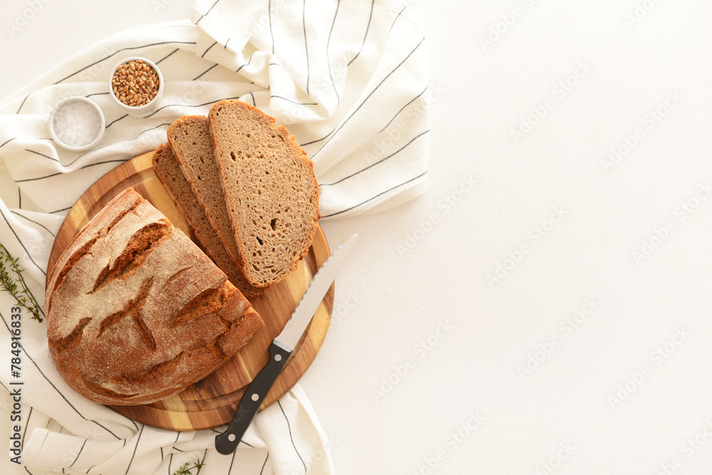 Fototapeta premium Wooden board with sliced loaf of bread, wheat grains, thyme and knife on white background