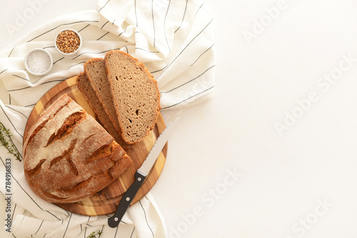 Wooden board with sliced loaf of bread, wheat grains, thyme and knife on white background © Pixel-Shot