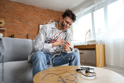 Obraz na plátne Electrocuted young man with burnt face and wires sitting on sofa at home