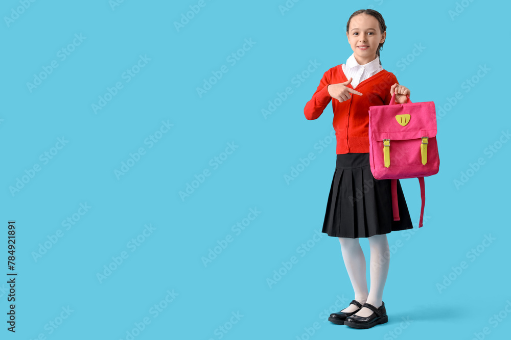 Happy little schoolgirl pointing at backpack on blue background Happy little schoolgirl pointing at backpack on blue background
