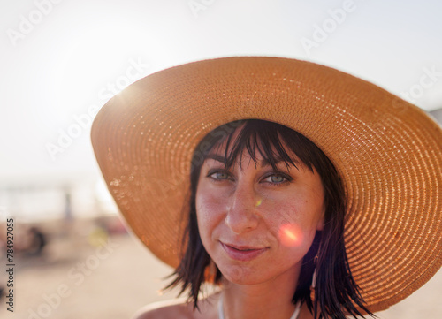 Close-up of the face of an attractive girl wearing a straw hat. Portrait of a happy young woman in a summer hat with a large brim on the beach.