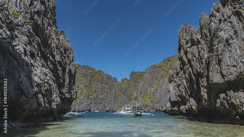 Traditional Filipino double-outrigger dugout  bangka  boats are anchored in a lagoon surrounded by picturesque karst rocks. Green vegetation on steep slopes. Clear blue sky. Philippines. Secret lagoon