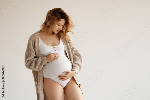 A beautiful pregnant girl in a white bodysuit and an oversized jacket, wavy hair. A pregnant beauty is expecting the birth of a child. Clothes for pregnant women, copy space. Motherhood and Childhood © looking2thesky