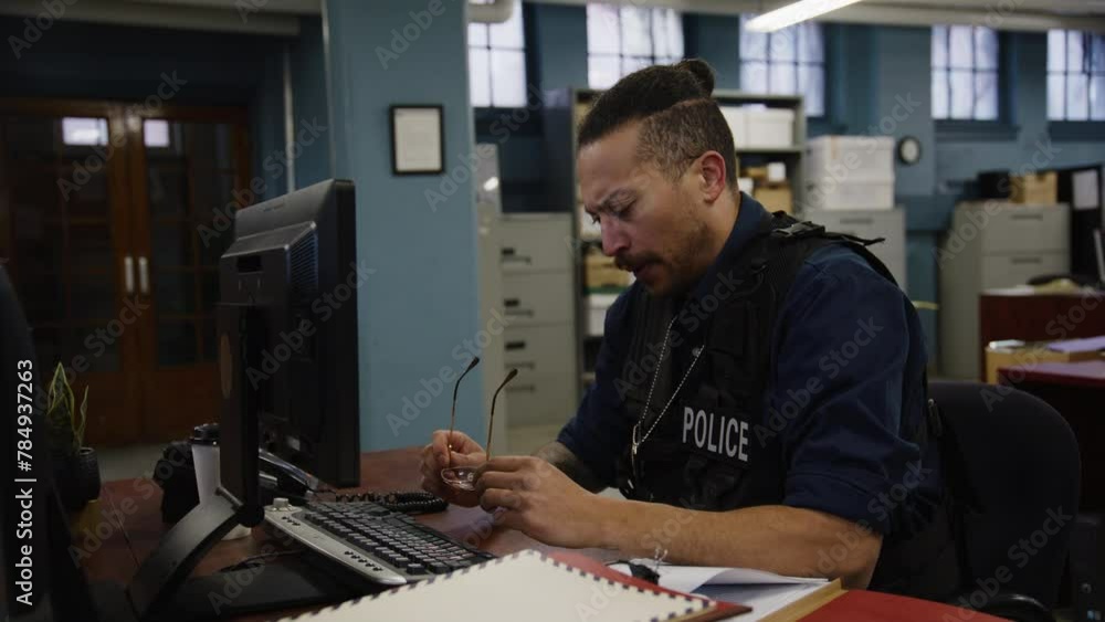 Police officer in a bullpen on computer tired Police officer in a bullpen on computer tired