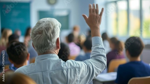 Back view of older student raising his hand to answer teacher's question during education training class