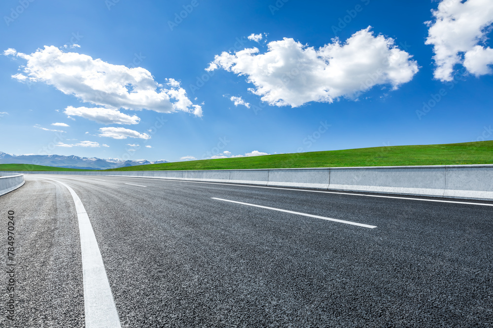 Asphalt highway road and green meadow with mountain nature landscape on sunny day Asphalt highway road and green meadow with mountain nature landscape on sunny day