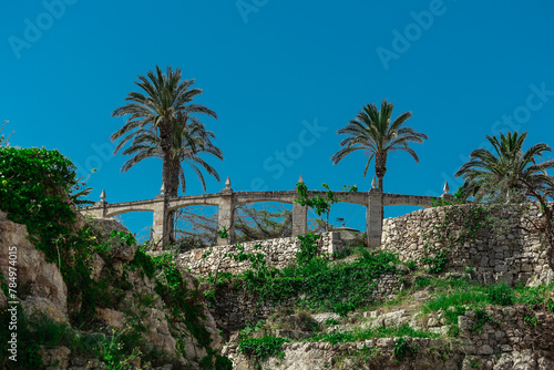Remains of old buildings at Polignano a mare, picturesque italian coastal town in Puglia, blue skies and palms ar visible rising above something which looks like a bridge