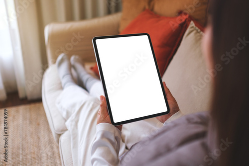 Mockup image of a woman holding digital tablet with blank desktop screen while sitting on a sofa at home