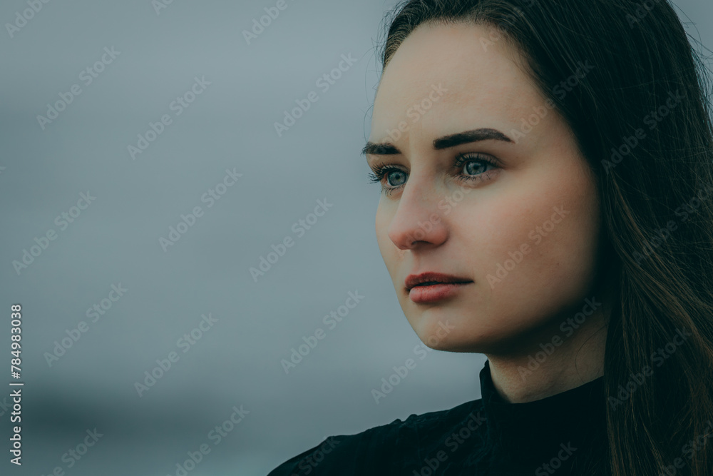 woman is sitting on a rocky shore with waves crashing behind her. Black dress, checkered coat. Cloudy sky. woman is sitting on a rocky shore with waves crashing behind her. Black dress, checkered coat. Cloudy sky.
