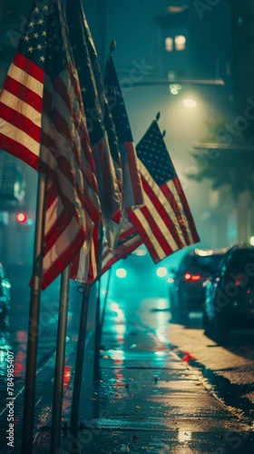 Wet American flags waving in the night with glowing city lights and parked cars backdrop