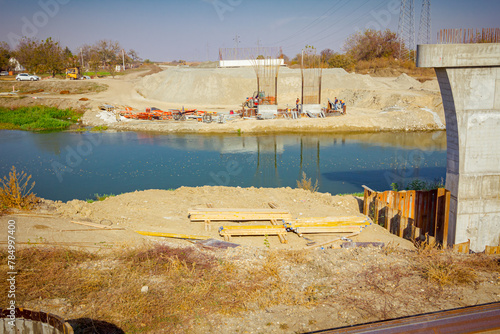 Pile of arranged boards placed on soil at the building site, over river are unfinished bridge poles