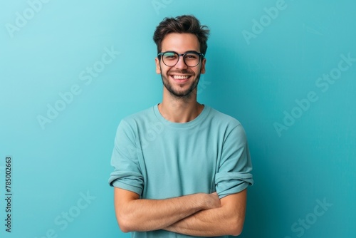 Portrait of a handsome young man in a glasses with a crossed arms in a studio plain background. AI generated