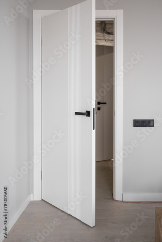 An open white door with a manual one in a renovated apartment. Moving to a new apartment. Doorknob on an open door with a ladder in the room during renovation and painting work.