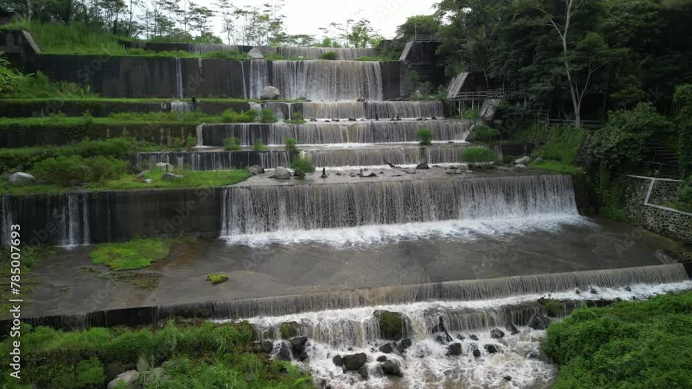 Grojogan Watu Purbo, Yogyakarta. Large multi-level dam on a river whose water is murky brownish due to mud during heavy rain surrounded by trees and meadows during overcast. Artificial Waterfall. Grojogan Watu Purbo, Yogyakarta. Large multi-level dam on a river whose water is murky brownish due to mud during heavy rain surrounded by trees and meadows during overcast. Artificial Waterfall.