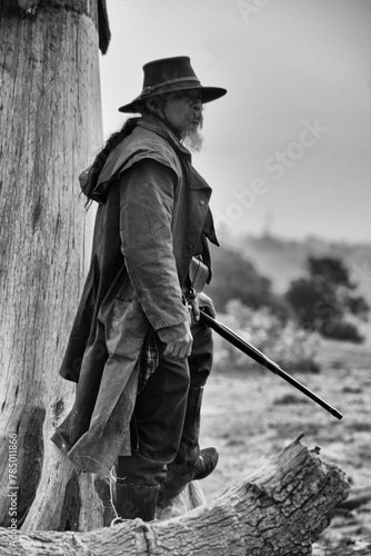 Black and white photo of a Mexican cowboy standing with gun in hand