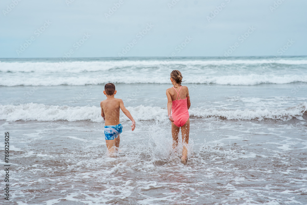 Siblings playing on beach, running, skipping, having fun on sandy beach of Canary islands. Concept of family beach summer vacation with kids.