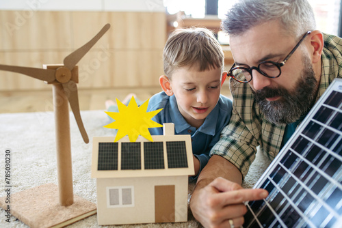 Father explaining renewable energy, solar power and teaching about sustainable lifestyle his young son. Playing with model of house with solar panels.