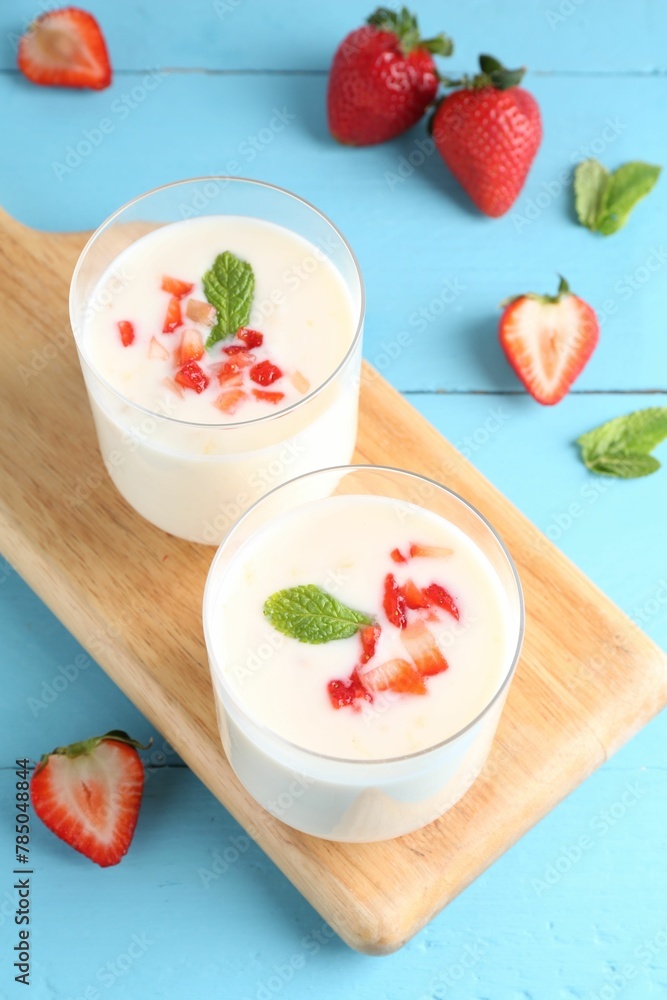 Tasty yogurt in glasses and strawberries on light blue wooden table Tasty yogurt in glasses and strawberries on light blue wooden table