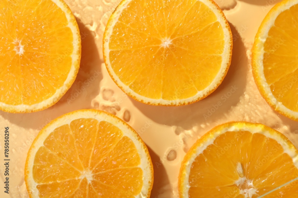 Fototapeta premium Slices of juicy orange and water on beige background, flat lay