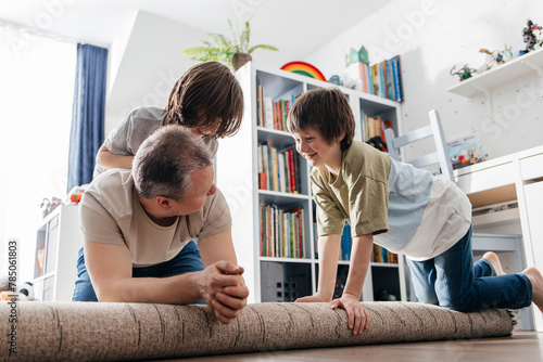 Happy children playing with father on rolled up carpet at home photo
