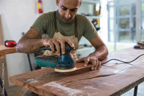 Carpenter polishing wooden piece with sander machine at workshop photo