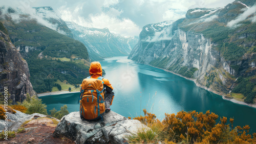 Traveler with backpack gazes at lake from rock in natural landscape photo
