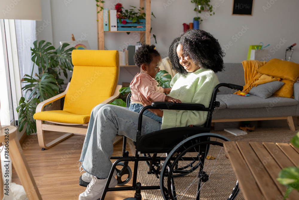 Baby girl sitting on smiling mother with disability in wheelchair at home Baby girl sitting on smiling mother with disability in wheelchair at home