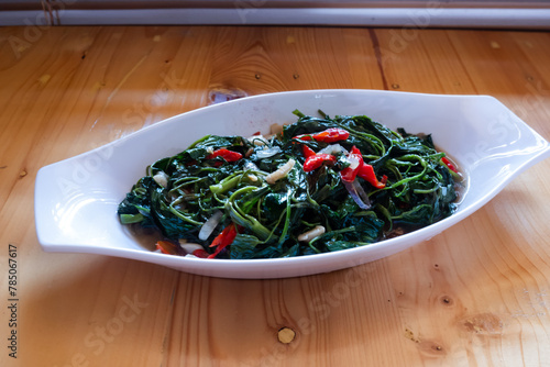 Stir fried water spinach or "tumis kangkung" indonesian food served on white oval plate on wooden table.